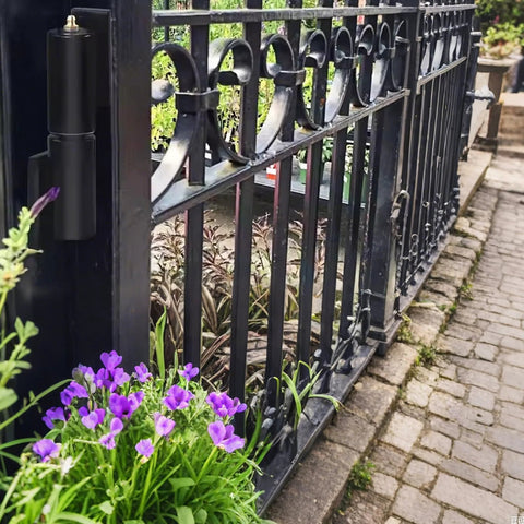 Gate hinge mounted on black ornate iron fence beside a stone walkway