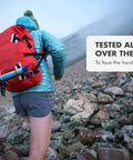 Hiker with red backpack showing personal water purifier for hiking camping travel and emergency prep on rocky terrain.