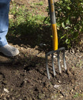 Person using 4 Tine Forged Spading Fork With 30 Inch Hardwood Handle And Poly D Grip For Maximum Leverage in garden soil