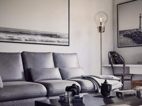 Edison Floor Lamp In Antique Brass Finish, Clear Glass Shade standing next to gray sofa in modern living room setting.