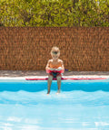 Child sitting by pool with Brown 6 Ft Reed Fencing Roll 16.4 Ft Long Outdoor Privacy Screen for balcony patio yard garden wind block.