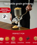 Heavy Duty Cast Iron Grain Mill With High Hopper Manual Crank Grinder For Corn Rice Soybeans Pepper Chickpeas And More Ideal For Domestic Use And Traditional Home Kitchen Milling For Home Cooks on a wooden surface, showing adjustable plates and grains.