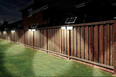 Solar Powered AI Smart Motion Dual Head LED Flood Light 10W 1200 Lumens Outdoor Security Glow illuminating a wooden fence