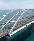 Aerial view of a modern cable-stayed bridge spanning over blue water on a clear day.