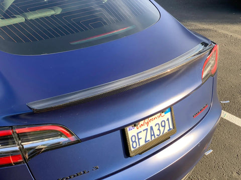 Real Molded Carbon Fiber Matte Dry Look Spoiler For Tesla Model 3 installed on blue car, showcasing aerodynamic design and sleek style.