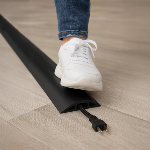 Person stepping over D-2 Rubber Duct Cord Cover, 36 Inch Black Floor Cable Protector for home office setup on wooden floor.