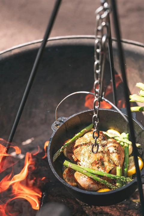 Rugged Heavy Duty Steel Camping Tripod For Open Fire Cooking suspends Dutch oven over flames with chicken and asparagus