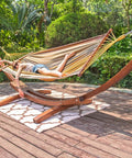 Two Person Cotton Fabric Hammock With Spreader Bars And 10.5 Ft Wood Arc Stand set up on patio with person lounging