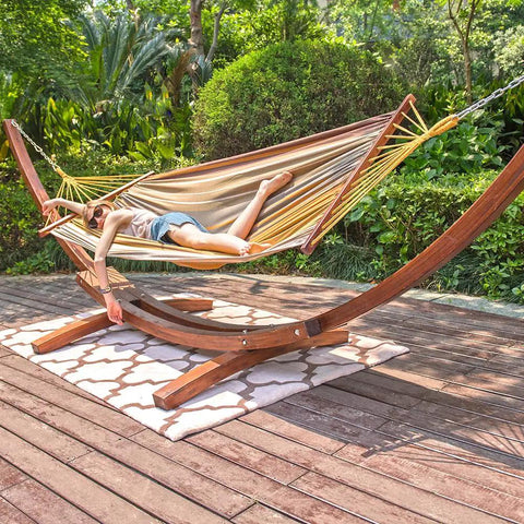 Two Person Cotton Fabric Hammock With Spreader Bars And 10.5 Ft Wood Arc Stand set up on patio with person lounging