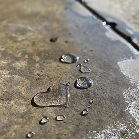 Water droplets forming a heart shape on a sealed concrete surface, illustrating Penetrating Siloxane PD Weather Seal For Concrete, Masonry, Stucco And Manufactured Stone Breathable Water Resistant Shield That Stops Cracking, Spalling, And Stains With 10 Year Service Life, 1 Gallon.