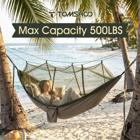 Person relaxing in a heavy duty camping hammock with built-in mosquito net and 500 lb capacity, on a beach between palm trees.