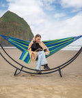 Heavy Duty Hammock Stand With Foldable Frame For Patio Hangout, Blue Green fabric, on beach, accommodates two to three people.