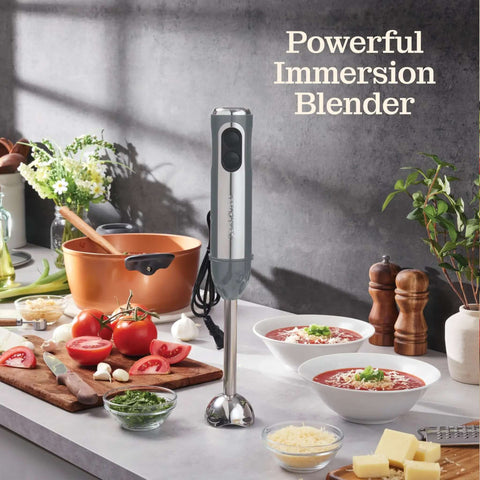 500 Watt Electric Hand Blender With Turbo Boost And Sharp Stainless Steel Blades For Smoothies Soups Purees And Baby Food Detachable Base Grey on kitchen counter with vegetables.