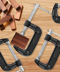 Beefy Eight Piece 2 Inch C Clamp Set, Heavy Duty Steel With Cast Iron Frame And Sliding T Handle, Built For Maximum Stability And Versatility In Woodworking, Welding, Building And Automotive Projects, Durable Black Finish. 2-inch black C clamps holding wood blocks on a bench.