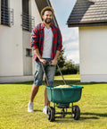 Man using 60 Lb Walk Behind Lawn Broadcast Spreader For Lawns And Gardens With Push Fertilizer And Grass Seed Spreading Adjustable Flow Control High Capacity Spreader For Fertilizer Or Seed Easy Refill on grass