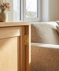 4 Pack 1 Inch Brass Butt Hinges For Wooden Boxes, mounted on a light wood cabinet door next to a beige sofa.