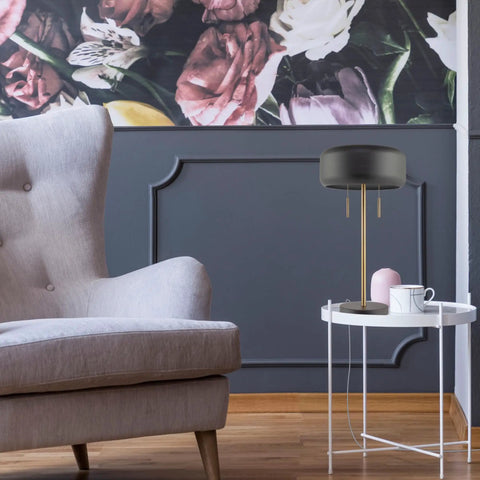 Modern black table lamp beside a gray armchair in a stylish living room with floral wallpaper