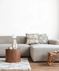 Modern living room with a beige sectional sofa, wooden coffee table, decorative pillows, and a small stool on a patterned rug.