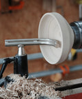 Side view of a white turned bowl on a metal wood lathe with a toolrest.