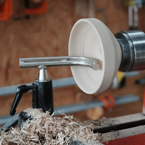 Side view of a white turned bowl on a metal wood lathe with a toolrest.