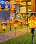 8 Pack Ultra Bright Solar Torch Lights With Flickering Flame installed along a garden pathway, waterproof in rainy weather.