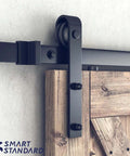 Close-up of heavy duty sliding barn door hardware kit with black finish and J shape hangers on installed wooden door panel.