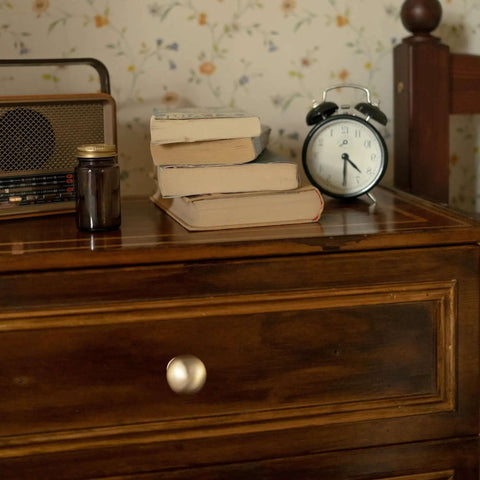 Bedroom nightstand with soft champagne bronze cabinet knob, radio, books, and an alarm clock
