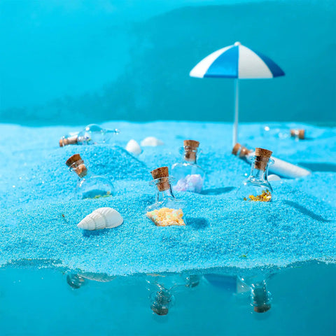 Big Time Favorite Mini Glass Jars With Cork Stoppers, 50 Pack Super Cute Wishing Bottles In 10 Unique Styles arranged on blue sand.