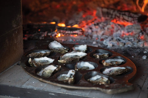 Cast Iron Oyster Grill Pan With 12 Cavities grilling oysters on an open flame, highlighting the black, heavy-duty nonstick surface.