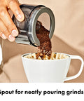 Compact Stainless Steel Conical Burr Electric Coffee Bean Grinder Delivers Smooth Daily Brews With Fine To Coarse Grinds pouring coffee grinds into a cup.