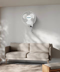 Living room with wall mounted 16-inch oscillating fan above sofa. Two Pack 16 Inch Oscillating Wall Mounted Fans With 90 Degree Wide Oscillation Quiet Operation And Three Speed Settings Indoor Air Cooling For Home Garage Office Shed And Grow Tents With Pull Cord Controls.