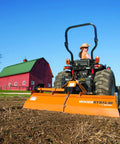 Farmer using rotary tiller on field with red barn in background