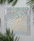 Close-up of Silver Bubble Envelope Mailer 15x13cm pack showing iridescent bubbles and self-seal edge on a textured surface.