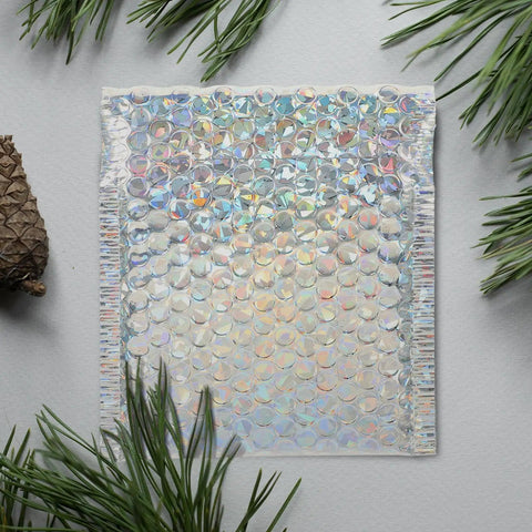 Close-up of Silver Bubble Envelope Mailer 15x13cm pack showing iridescent bubbles and self-seal edge on a textured surface.