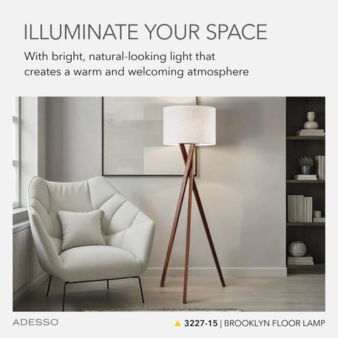 Living room with table lamp featuring walnut tripod base and white linen drum shade next to armchair.