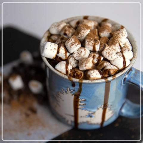 Hot chocolate topped with marshmallows in a blue mug created using 32 Oz Milk Frother And Hot Chocolate Maker With Cocoa Bomb Mold.