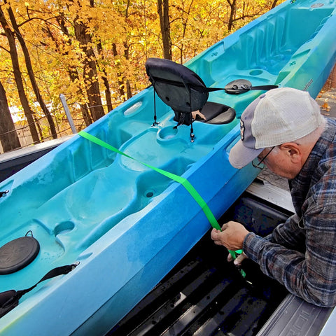 Person using Two Pack Truck Bed Anchor Kit For Tailgate with rugged polyester webbing to secure a blue kayak in a pickup truck bed.
