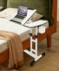 Smooth Rolling Standing Desk Heavy Duty Sit Stand Laptop Cart Adjustable Height Lockable Wheels next to a bed with a laptop.