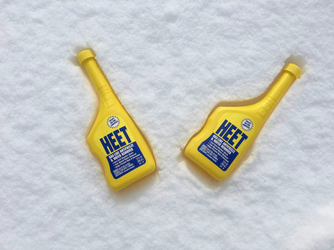 Two yellow bottles of Water Removal and Gas Line Antifreeze for Winter Starts Keeps Your Fuel System Free of Water Prevents Gas Line Freezing and Rust Protection Plus Easy Starts in Cold Weather 12 Fl Oz on snow.