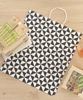 Vogue Tear-Resistant White Gift Bags With Built-In Handles, 100 Count, with black geometric print, shown on a wooden surface.