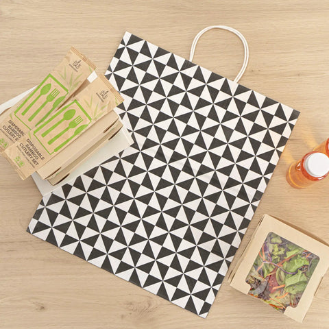 Vogue Tear-Resistant White Gift Bags With Built-In Handles, 100 Count, with black geometric print, shown on a wooden surface.
