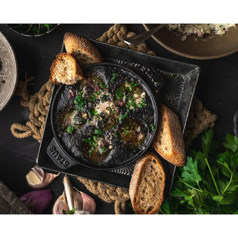 Top view of Cast Iron Escargot Dish With Six Holes, 5.75 Inch, Matte Black, Oven Safe To 500F, Brass Knob, with garnished escargot