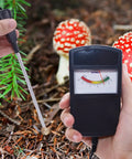 Person using Soil PH Tester Meter With Probe For Garden Lawn Farm Plants High Precision Quick PH Readings No Battery Needed Auto Power Long Lasting Acidity Gauge Tool For Gardens Orchards Vineyards Lawns Fields And Plant Care in a forest setting, mushrooms visible