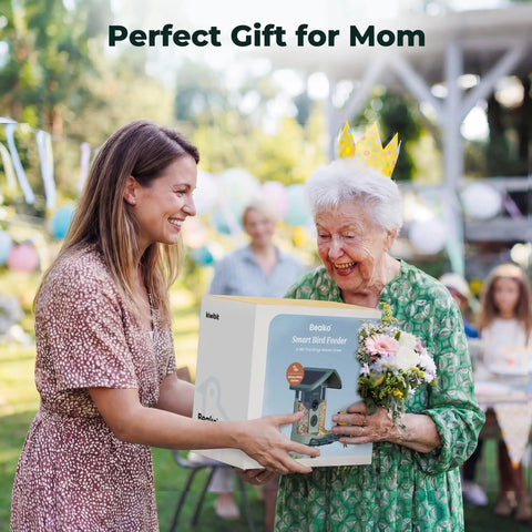 Two women outdoors smiling with a gift box of a Solar Powered Smart Bird Feeder With Camera AI Species ID 8MP Photos And 4K Ultra HD Video Live Stream For Outdoors Must Have Gift For Bird Lovers Easy Setup And Durable Green Feeder.