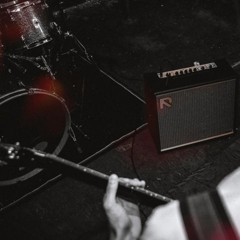 Musician playing guitar with 50 Watt Intelligent Guitar Combo Amp With Amp Intelligence on stage next to drum set