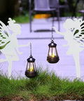 2 Pack Metal Fairy Hanging Lantern Solar Outdoor Garden Stakes with Silhouette Lights in nighttime garden setting