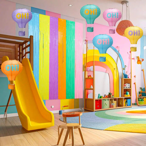Pastel Grad Party Decorations Kit with 6 printed hot air balloon paper lanterns and 2 tinsel foil fringe curtains in a playroom