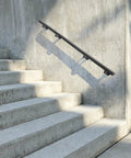 Heavy Duty Stainless Steel Flush Wall Mount Stair Railing secured to concrete stairs, matte black finish, supports two hundred pounds.