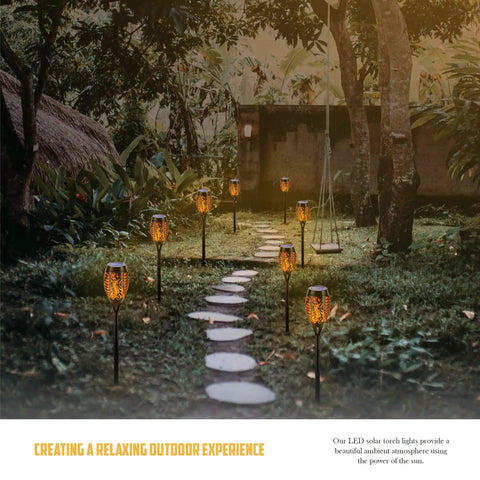 Outdoor Solar Flickering Torch Lights 8 Pack Waterproof Patio Tiki Lamps With 12 LED Flame Beams illuminating a garden path