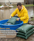 Person in yellow jacket submerging 5 Pack Flood Barrier Bags 16x24 Inches for Quick Water Control into blue container.